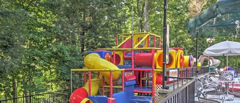 Un parque infantil con toboganes y estructuras para escalar, rodeado de árboles.