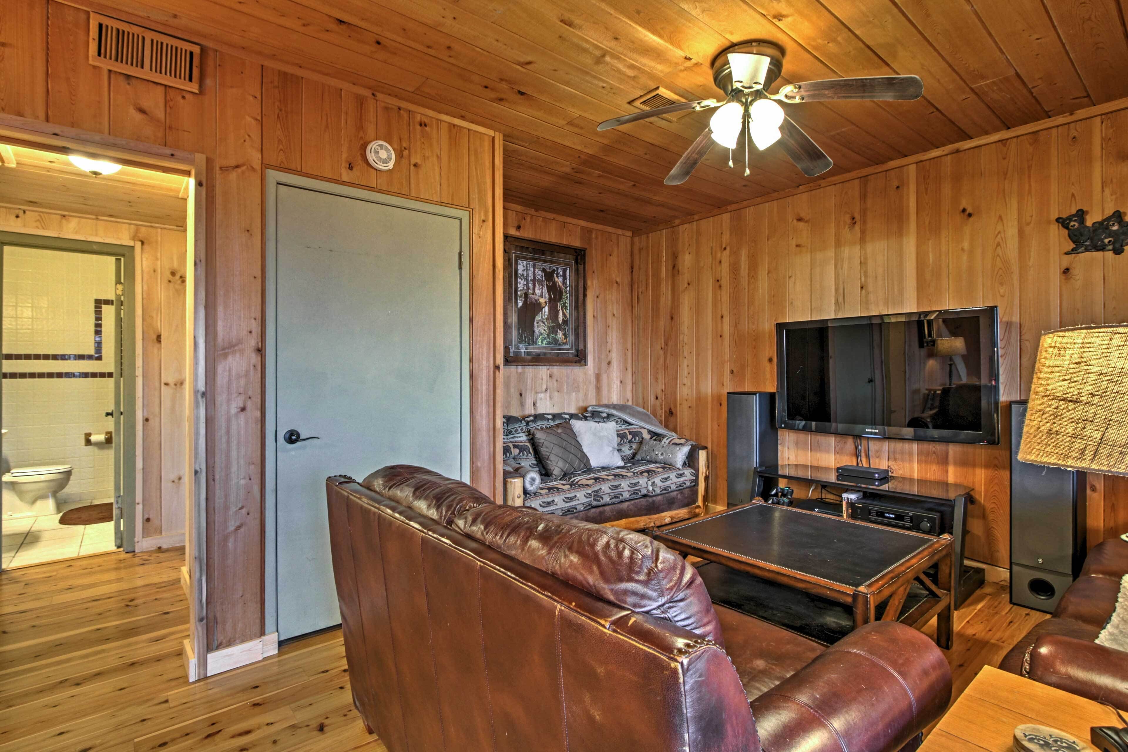 A wooden-paneled room with a leather sofa, a television, and a ceiling fan.