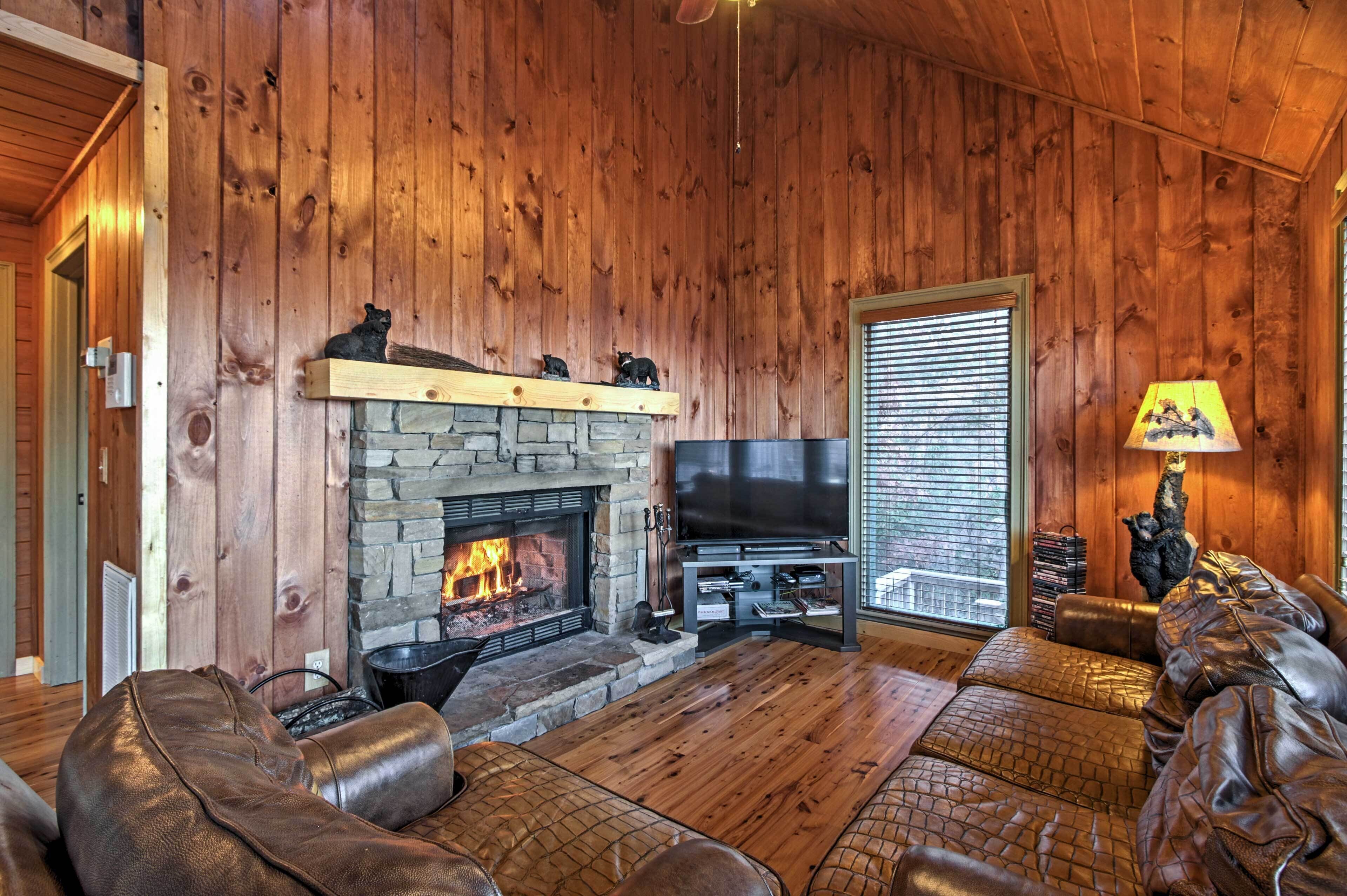 Ein gemütliches Wohnzimmer mit Kamin aus Stein, Ledersofas, einem Flachbildfernseher und einer Holzbalkendecke.