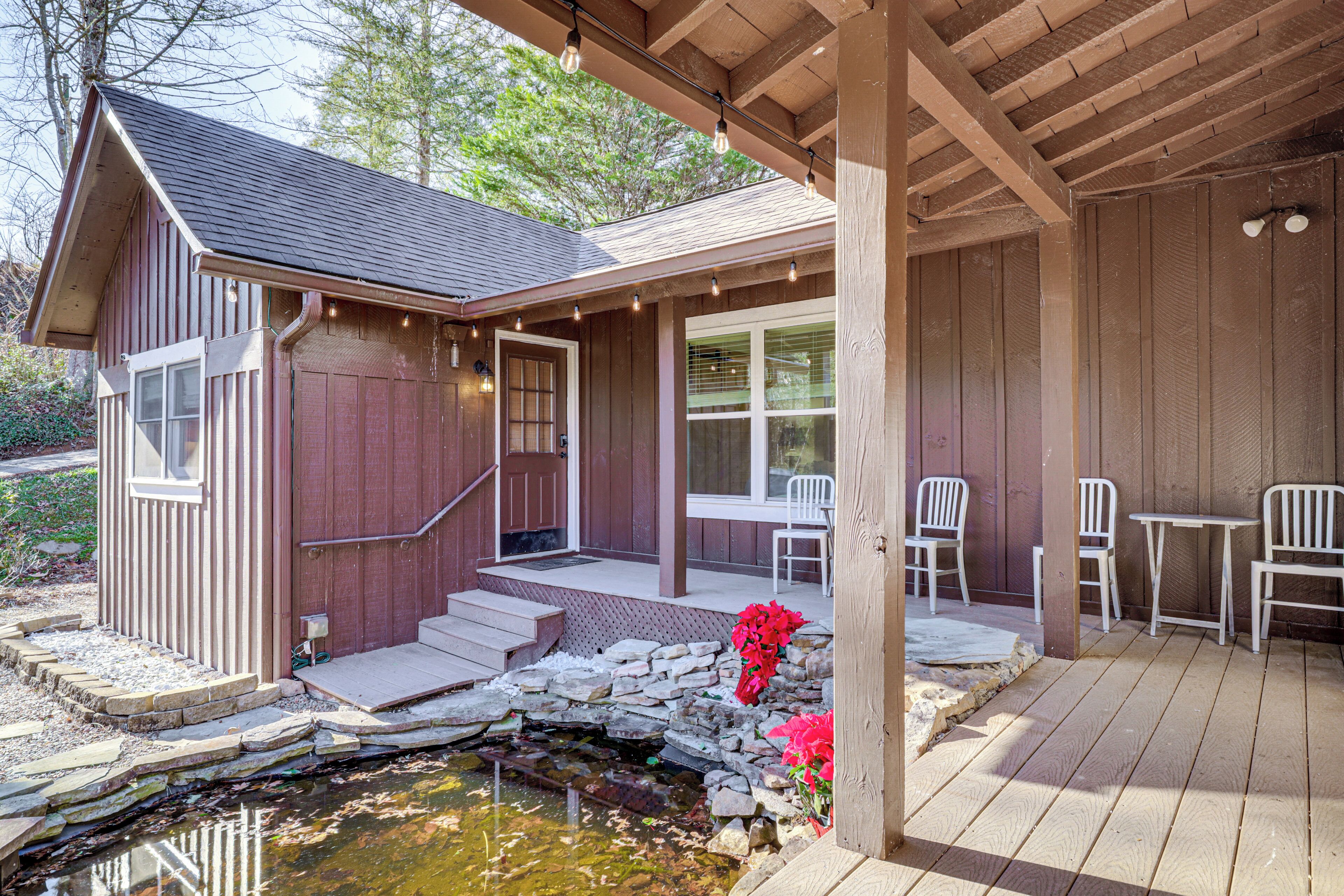 A wooden cabin with a porch, stone steps, a small pond, and outdoor seating.