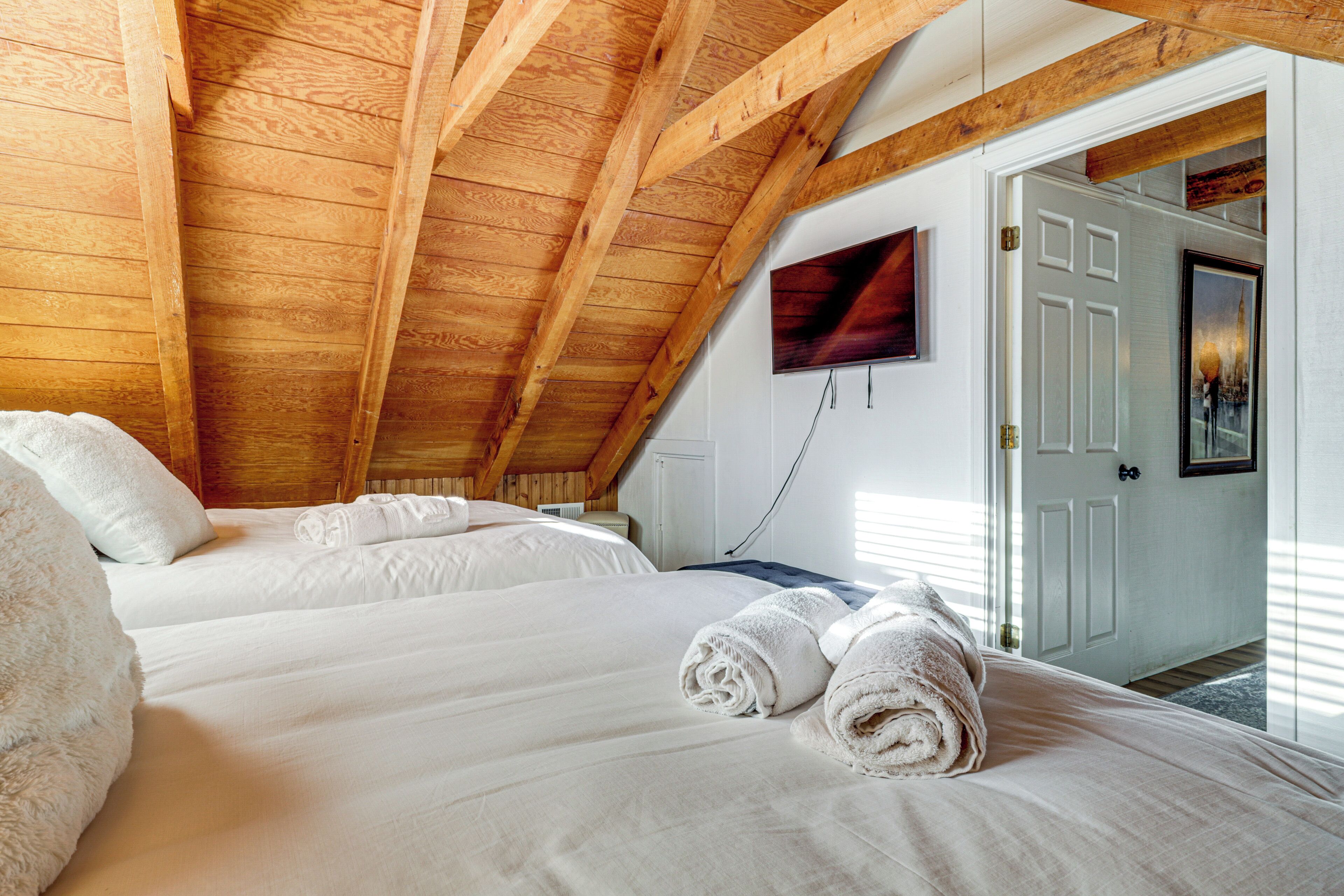 A bedroom with wooden beams, two beds, white linens, and rolled towels.