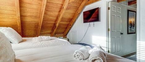 A bedroom with wooden beams, two beds, white linens, and rolled towels.