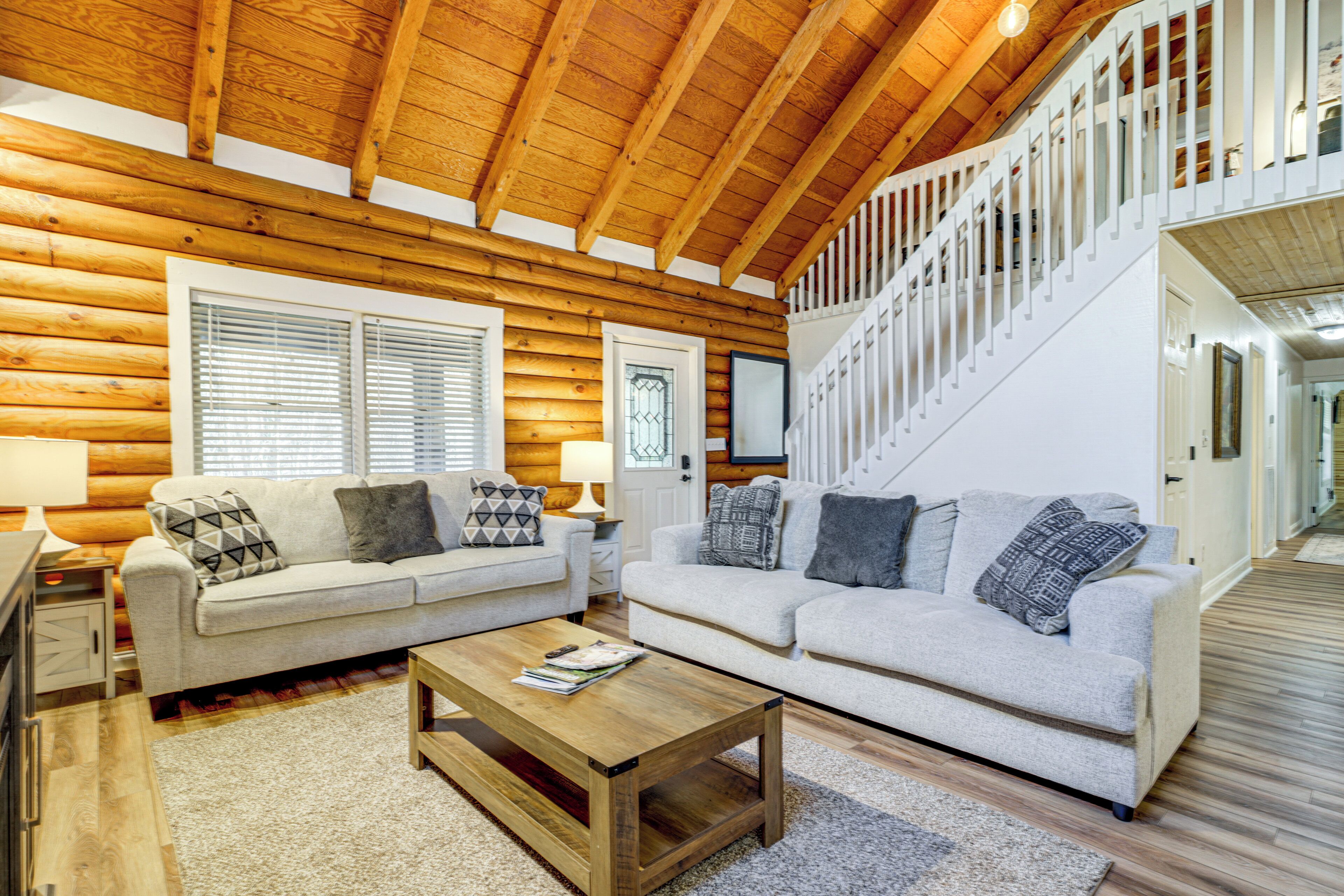 A log cabin interior with two sofas, a wooden coffee table, and a staircase.