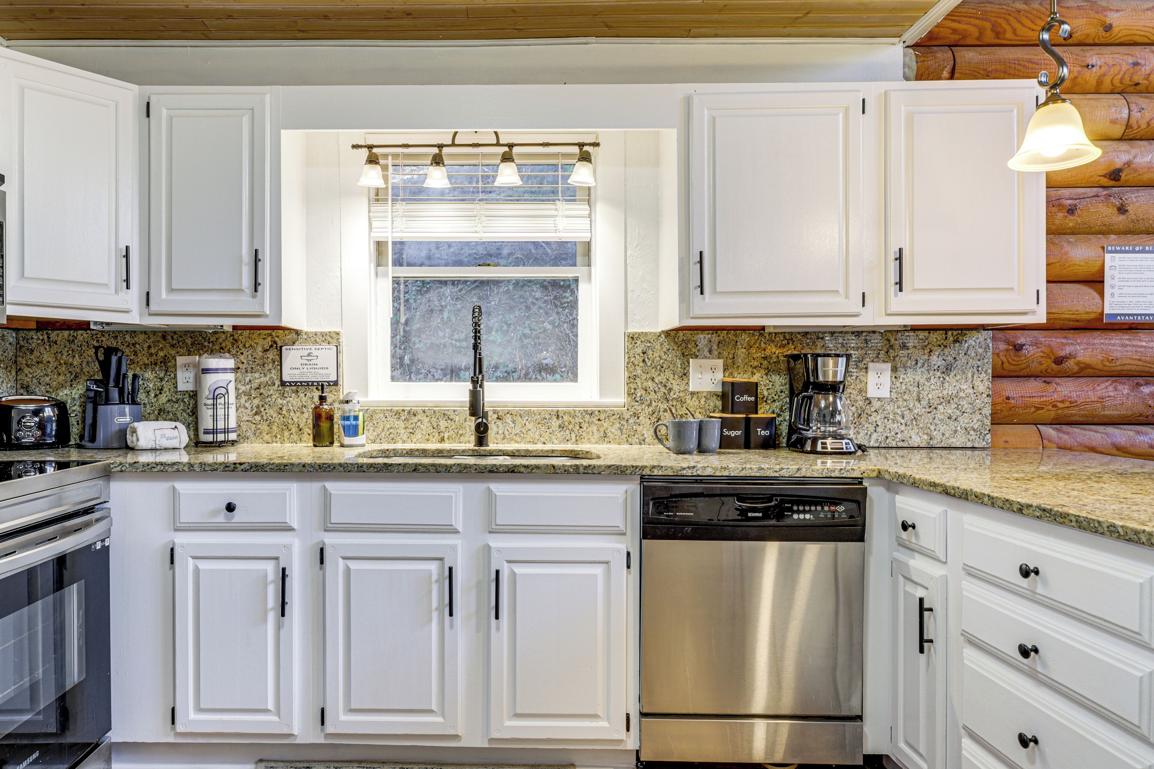 A kitchen with white cabinets, granite countertops, stainless steel appliances, and a window with blinds.