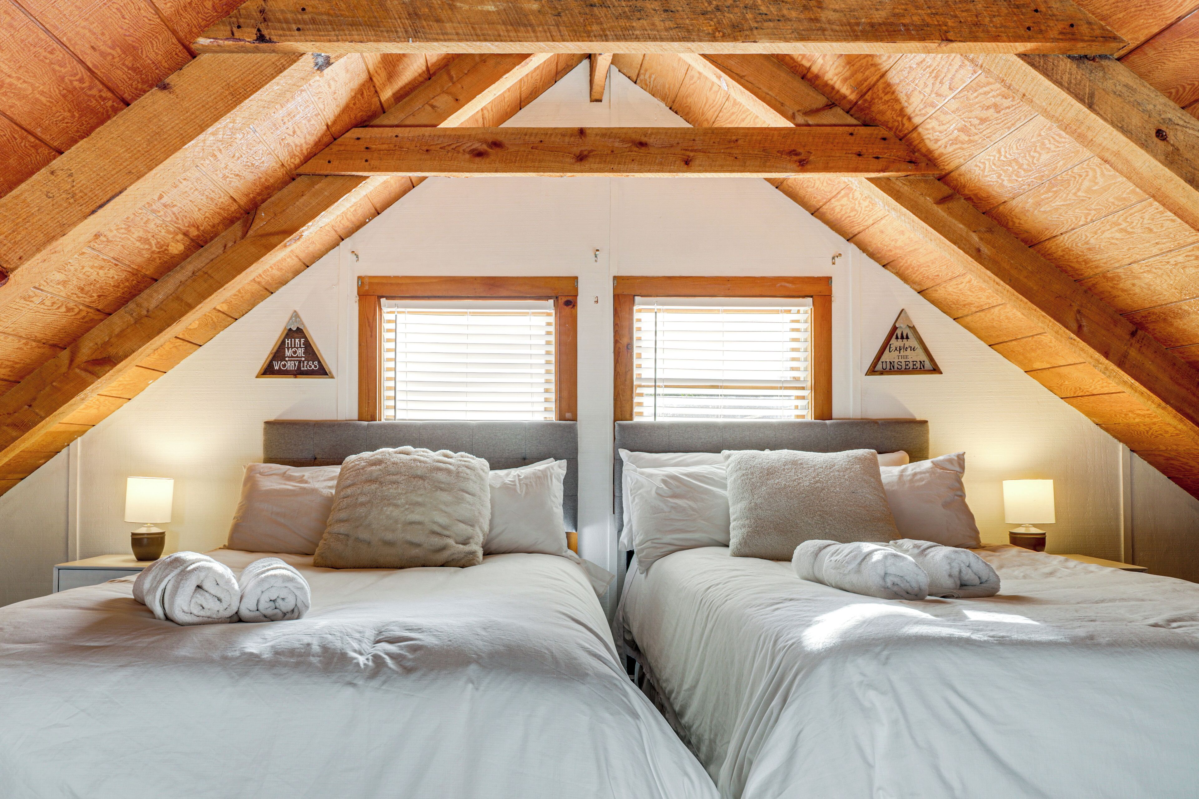 Ein Schlafzimmer mit zwei Betten, Holzbalken und zwei Fenstern mit Jalousien.