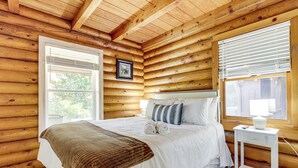 A log cabin bedroom with a large bed, a bedside table, and a window with blinds. - Pet-friendly Gatlinburg Cabin w/ Hot Tub! (Gatlinburg)