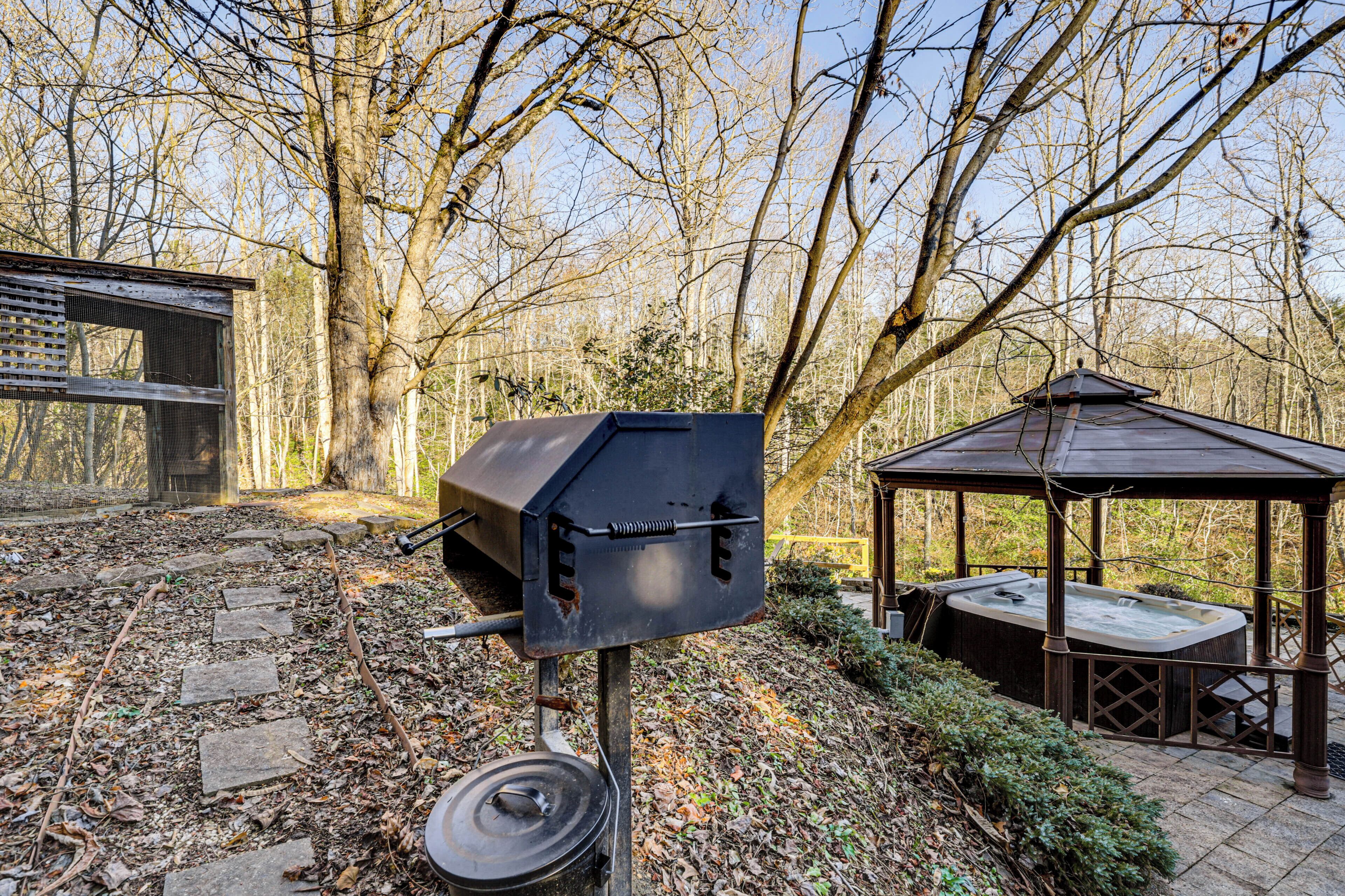 Un barbecue, un jacuzzi et un kiosque situés dans un espace boisé.