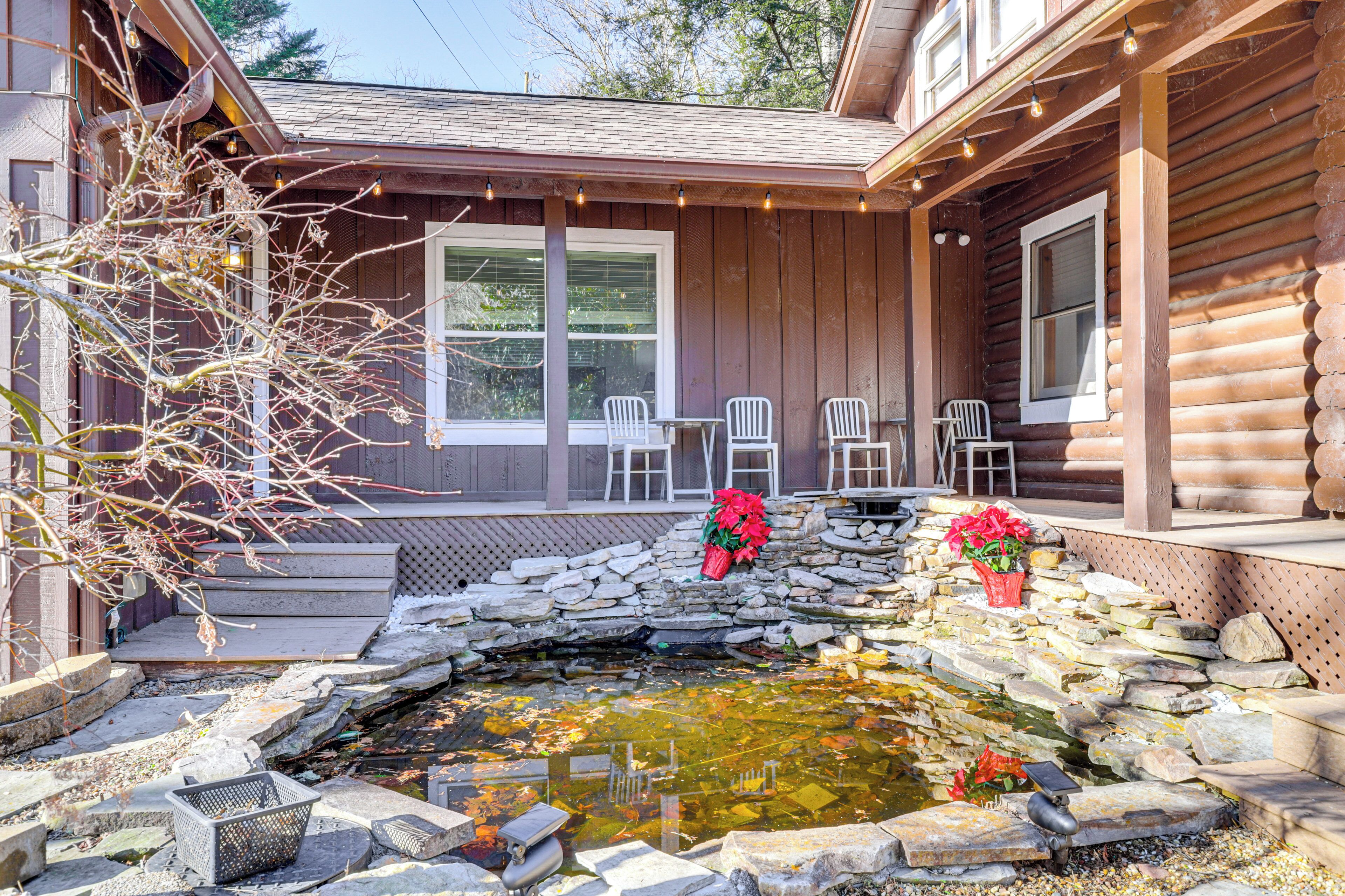 A wooden cabin with a stone pond, outdoor seating, and potted plants.