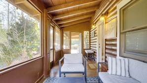 A log cabin interior with a wooden ceiling, a sofa, a chair, and a view of the outdoors. - Pet-friendly Gatlinburg Cabin w/ Hot Tub! (Gatlinburg)