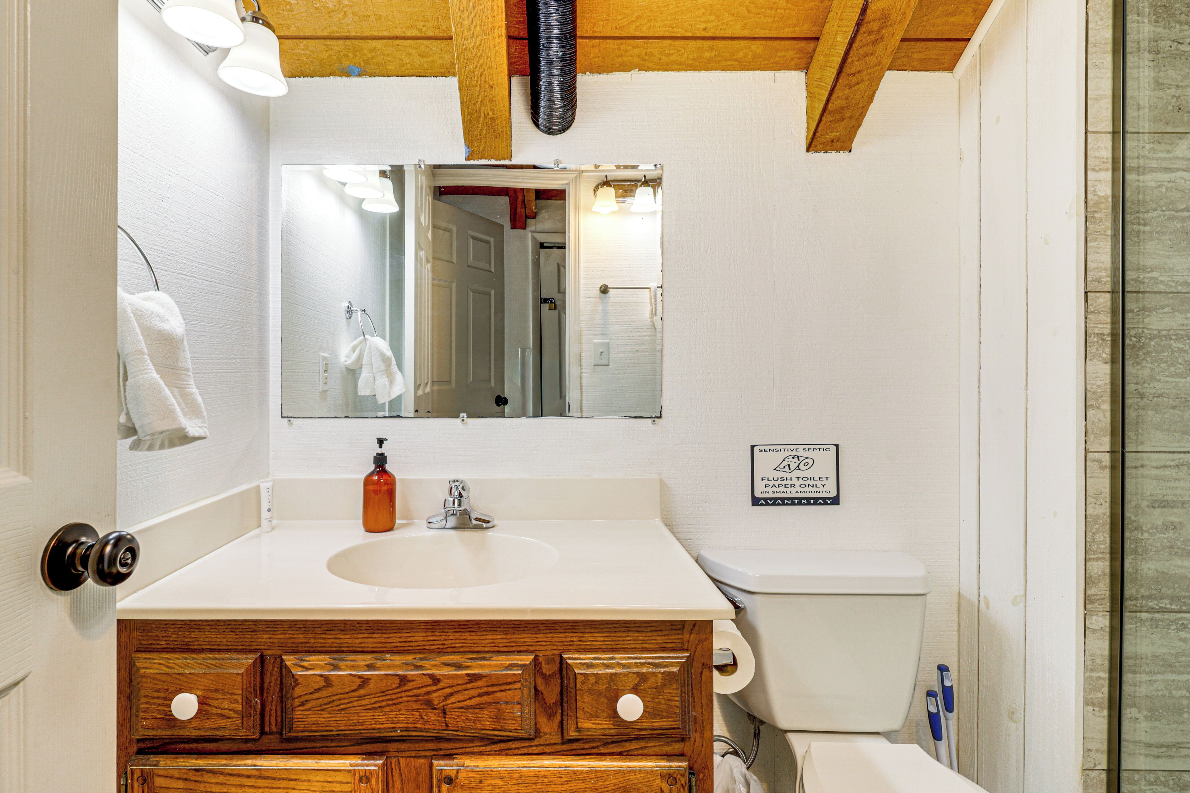 Ein Badezimmer mit einem Holzkosmetikschrank, einem weißen Waschbecken und einem Spiegel darüber. Ein Schild an der Wand weist auf die Nutzung der Toilette hin.