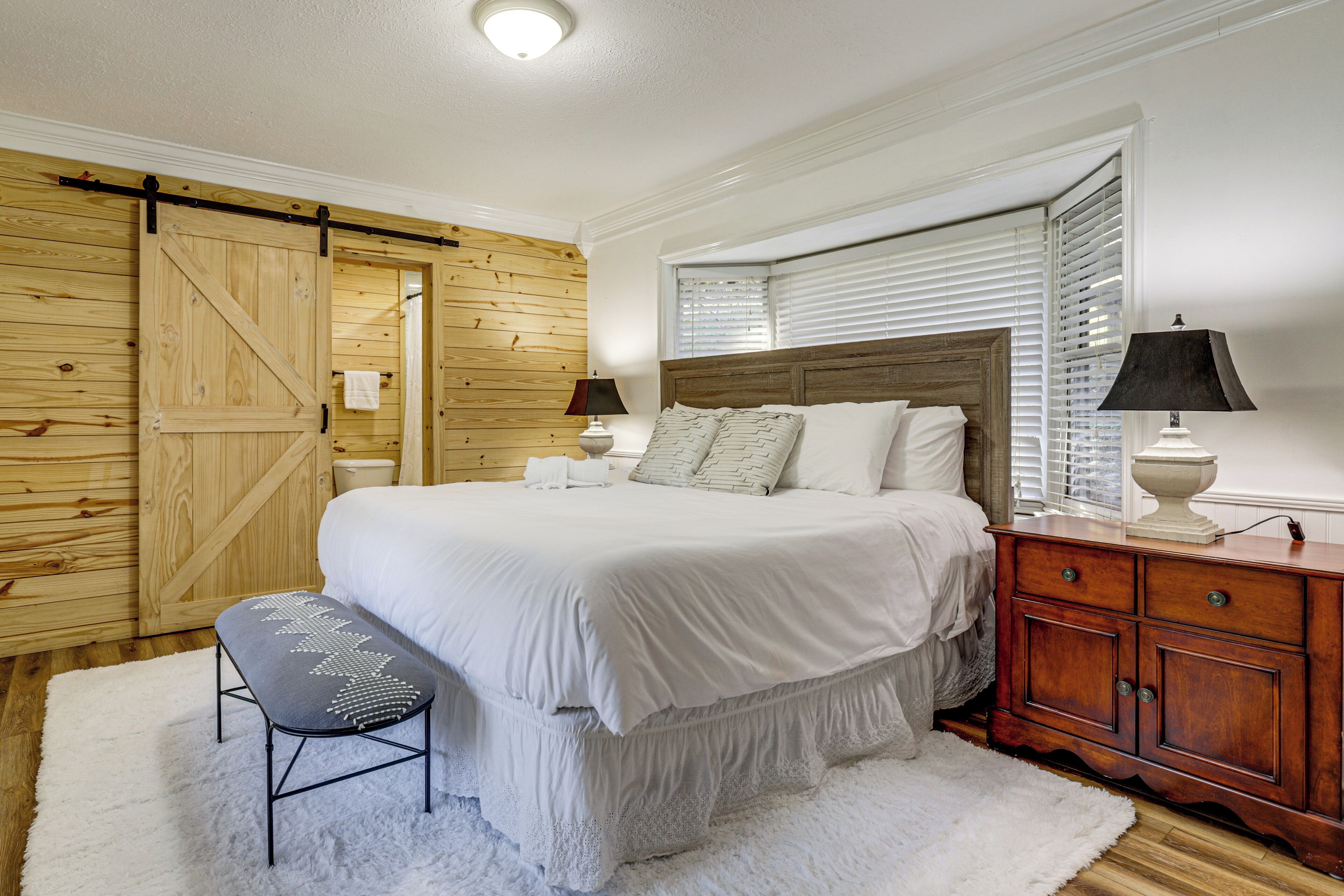 A bedroom with a bed, wooden wardrobe, bench, and two bedside tables with lamps.