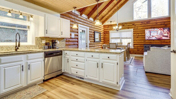A spacious kitchen with wooden log walls, white cabinets, and a large island. - Pet-friendly Gatlinburg Cabin w/ Hot Tub! (Gatlinburg)