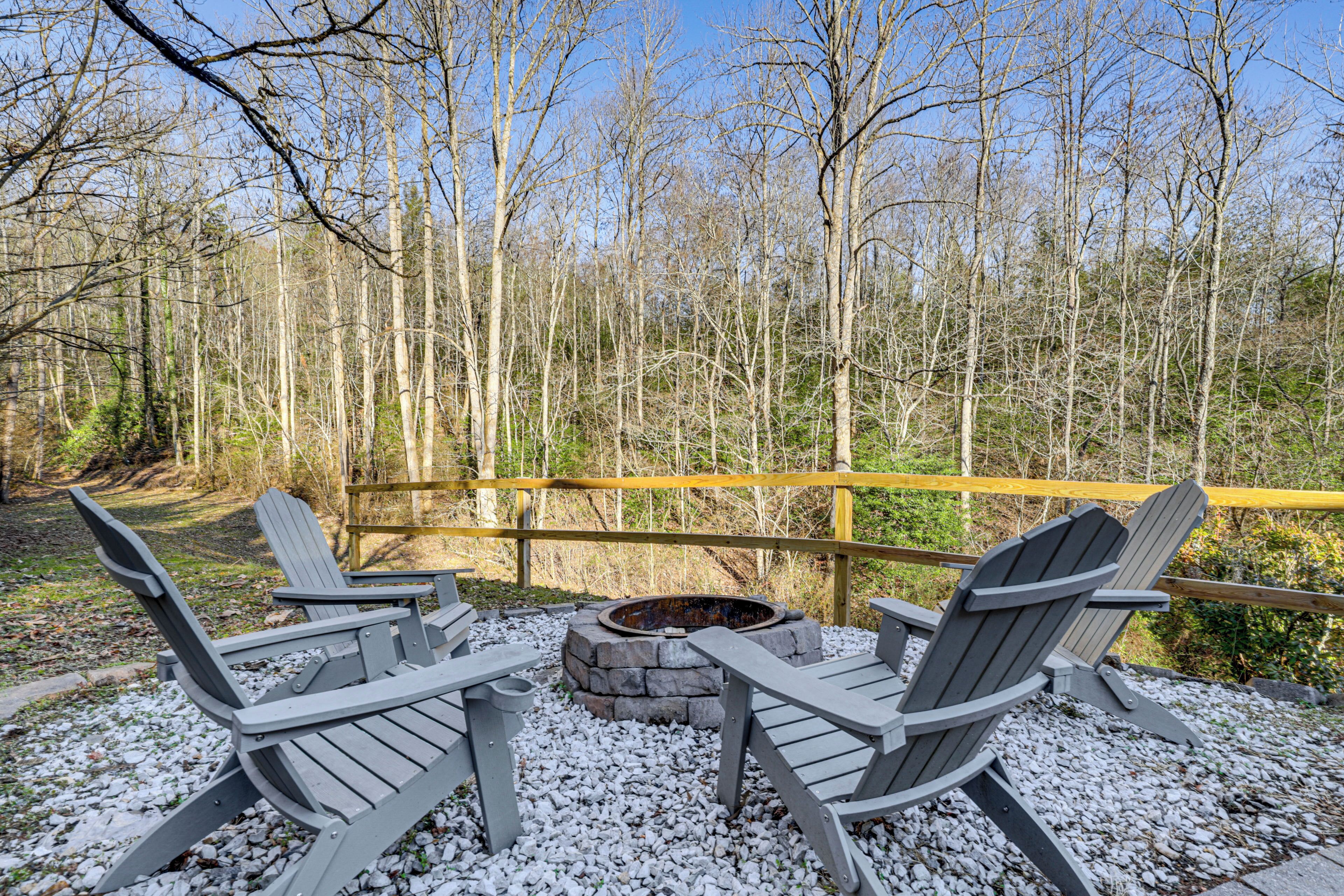 Une terrasse en bois, dotée de chaises Adirondack et d’un foyer en pierre, le tout entouré d’une forêt.