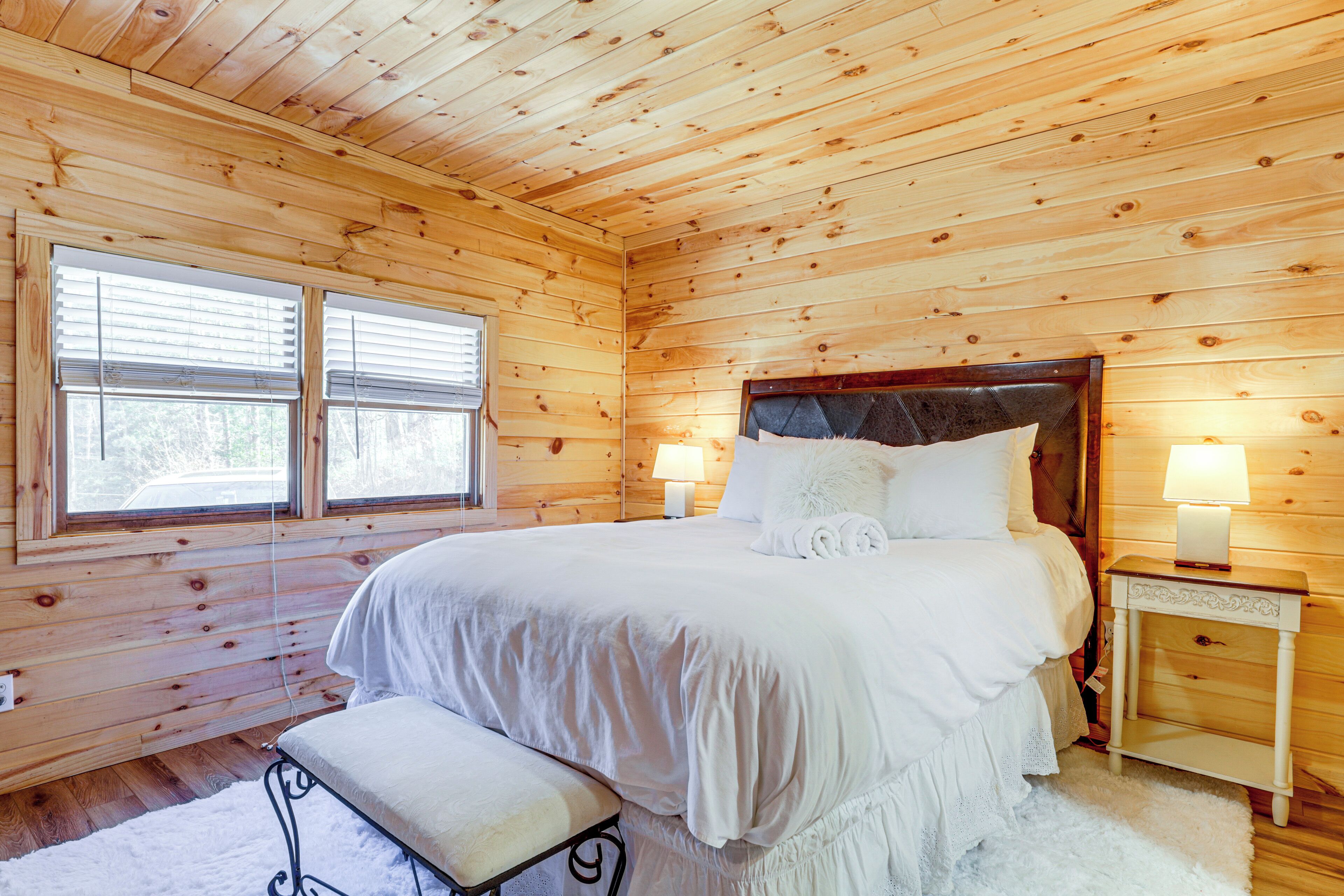 Un dormitorio con paneles de madera, una cama, lámparas de noche y un banco.