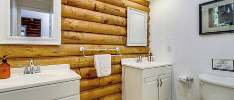 A bathroom with wooden log wall, white cabinets, a sink, and a toilet.