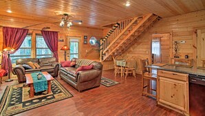 Un acogedor interior de cabaña con escalera de madera, sofás de cuero, zona de comedor y cocina.