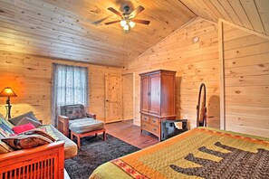A cozy log cabin room with a wooden ceiling, a ceiling fan, a bed with a quilt, a wooden cabinet, a chair, and a small table. - Creekside Cabin w/ Hot Tub in Gatlinburg! (Gatlinburg)
