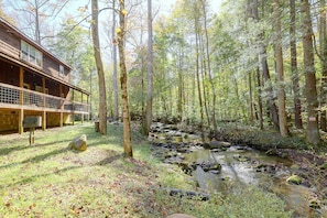A cabin with a deck overlooking a forest and a stream. - Creekside Cabin w/ Hot Tub in Gatlinburg! (Gatlinburg)
