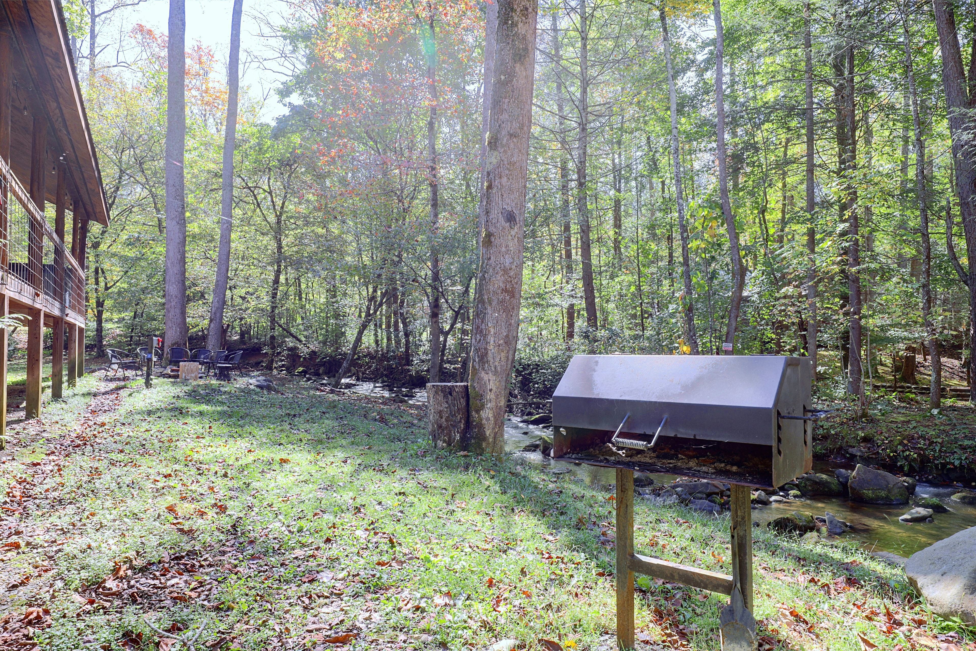 A forested area with a barbecue grill and outdoor seating.