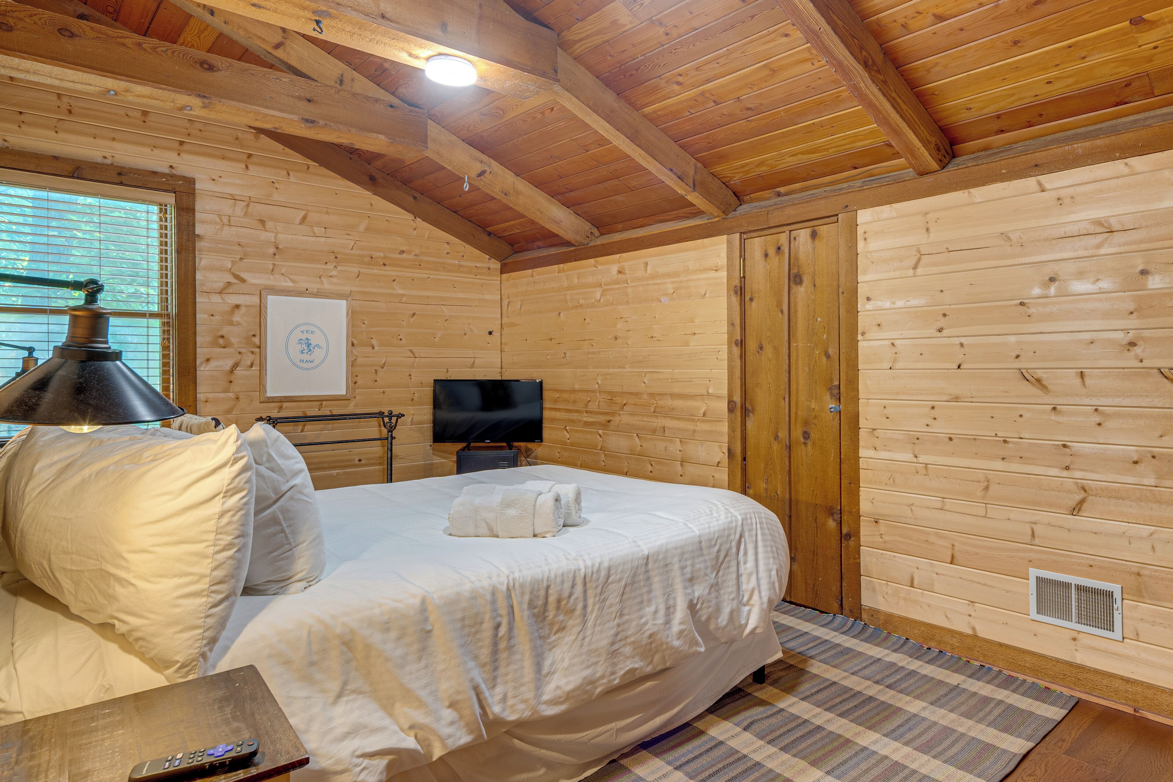 Een kamer met houten lambrisering, een bed, een televisie en een raam.