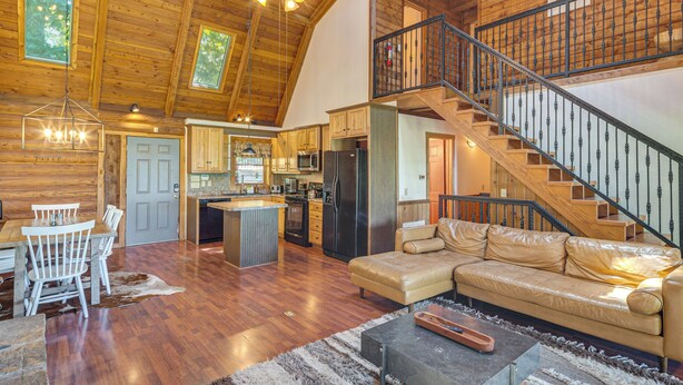 Un vaste espace de vie doté d’un plafond haut, d’un décor intérieur en bois, d’un îlot central et d’un escalier avec une rampe en métal.