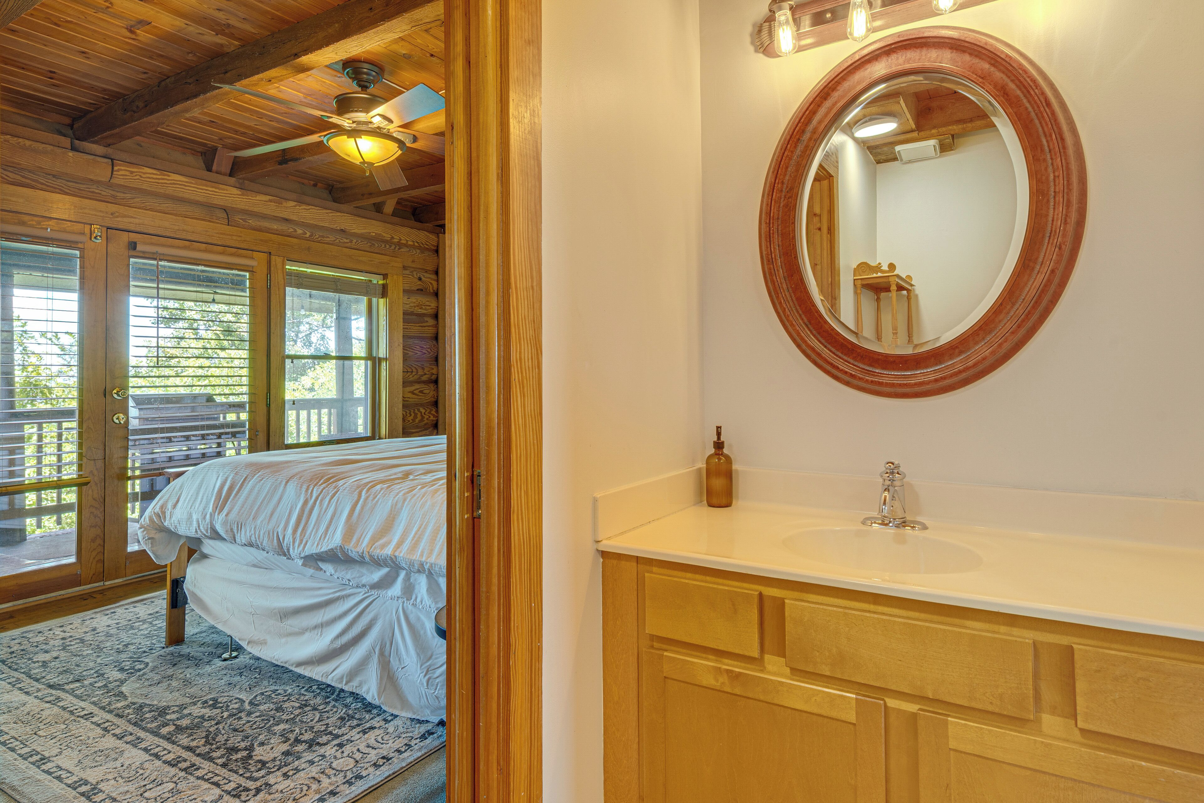 A bedroom with a bed, a wooden ceiling, a window, and a bathroom with a sink and mirror.
