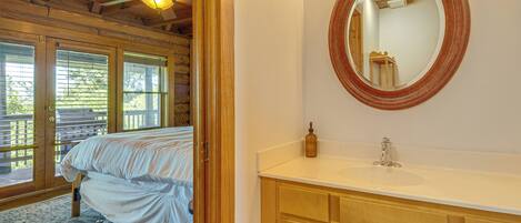A bedroom with a bed, a wooden ceiling, a window, and a bathroom with a sink and mirror.
