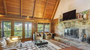 L’intérieur d’une cabane en rondins, avec une cheminée en pierre, des canapés en cuir et un téléviseur fixé au-dessus de la cheminée.