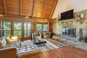A log cabin interior with a stone fireplace, leather sofas, and a television mounted above it. - 2 Mi to Ober Mtn: Hot Tub & Deck at Cozy Cabin! (Gatlinburg)