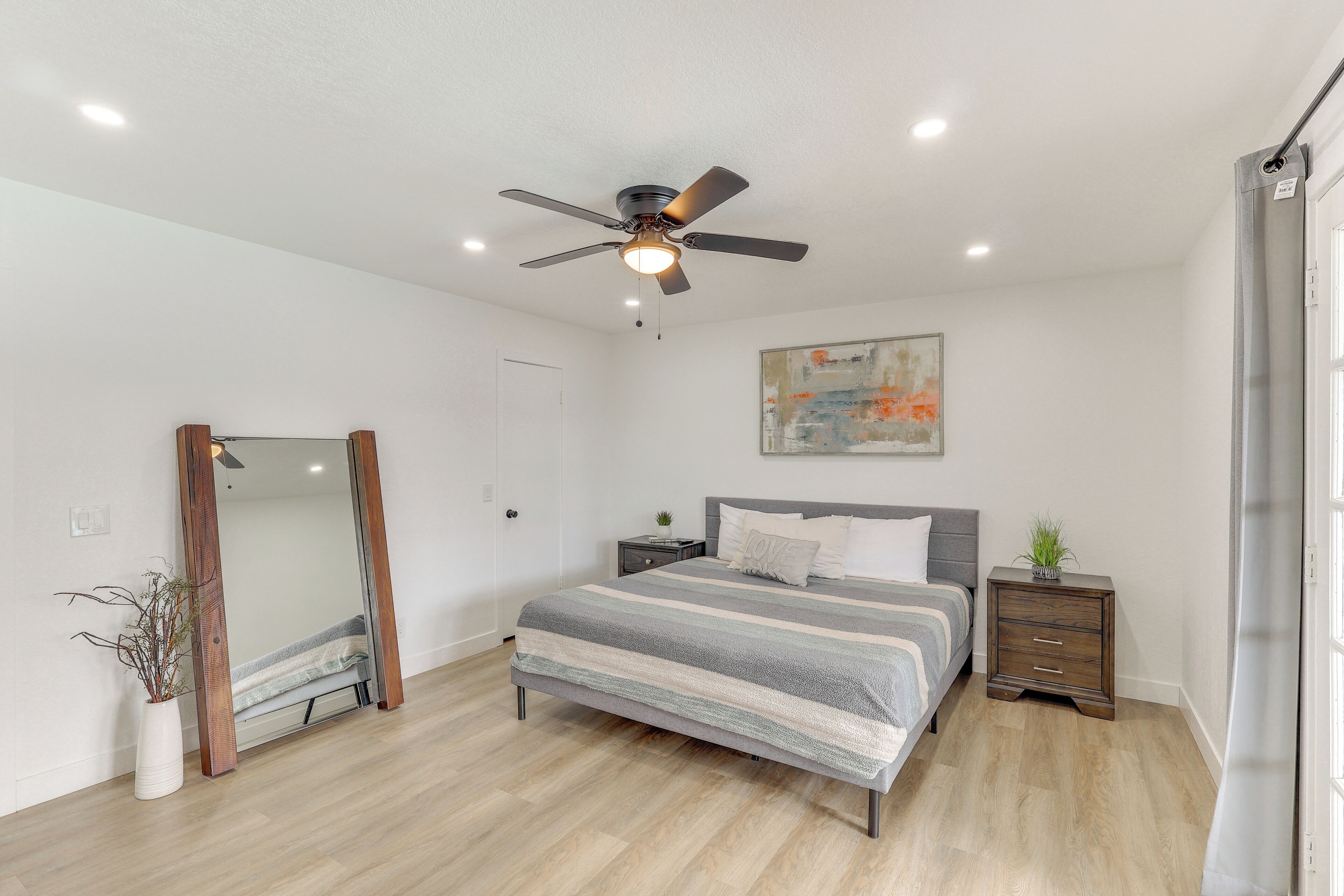 Ein Schlafzimmer mit Bett, Deckenventilator, Nachttisch, Spiegel und einem Gemälde an der Wand.
