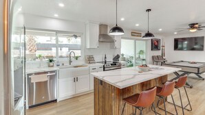 Une cuisine moderne avec des meubles blancs, des appareils en acier inoxydable et un îlot central en bois doté de tabourets de bar.