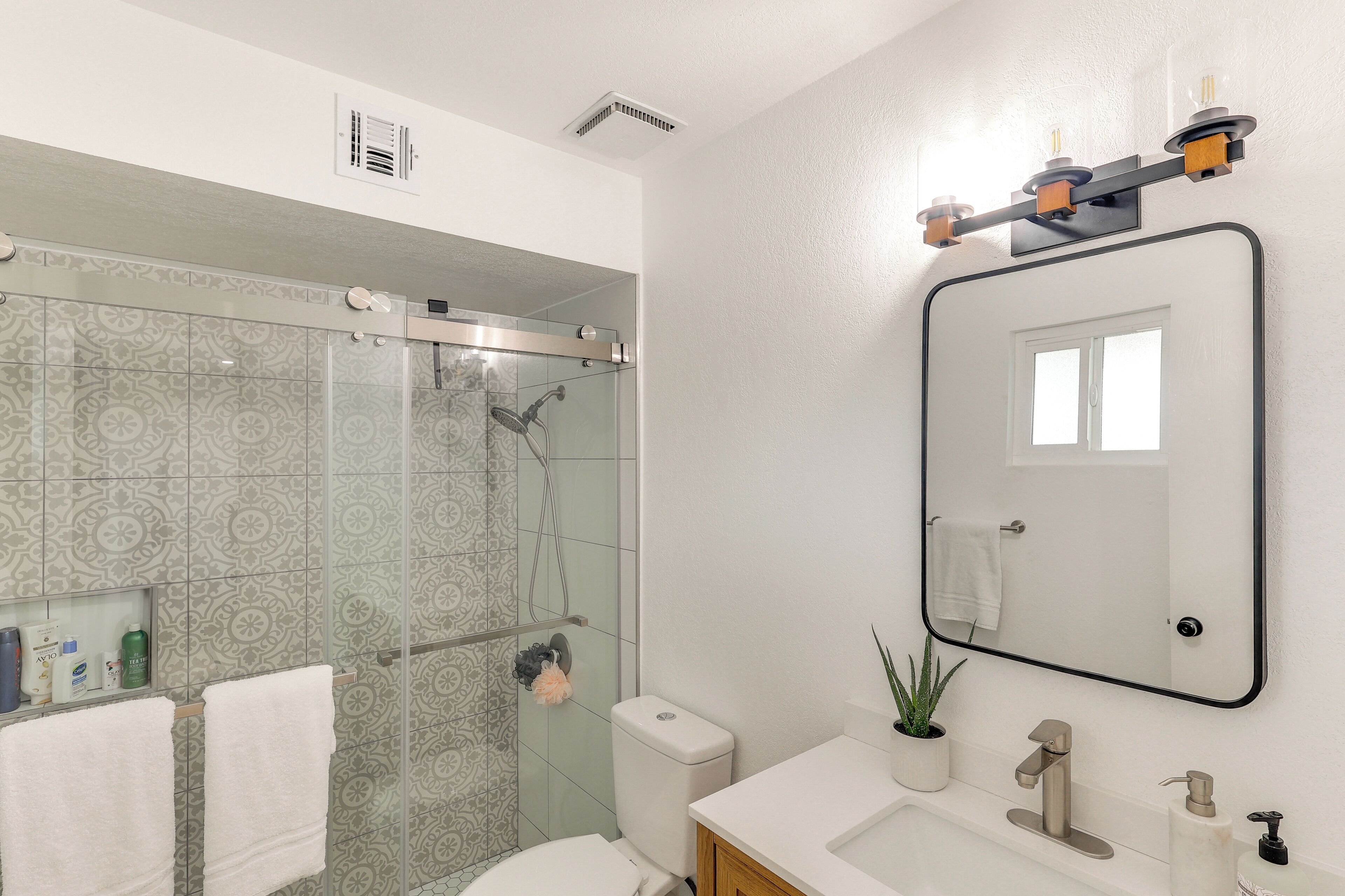 A modern bathroom with a glass shower enclosure, a white toilet, a vanity with a mirror, and a sink.