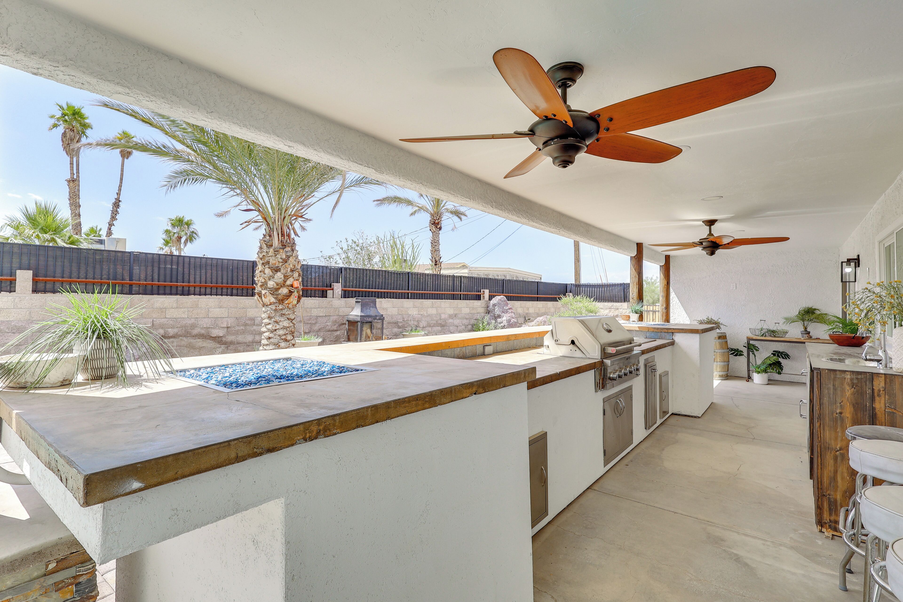 An outdoor kitchen area with a bar, ceiling fans, and a view of palm trees.