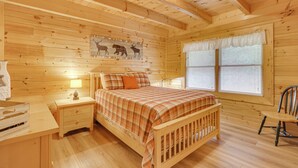 A wooden cabin bedroom with a bed, nightstand, lamp, and a window with blinds. - Private Hot Tub: Lake Resort Cabin in Sevierville! (Sevierville)