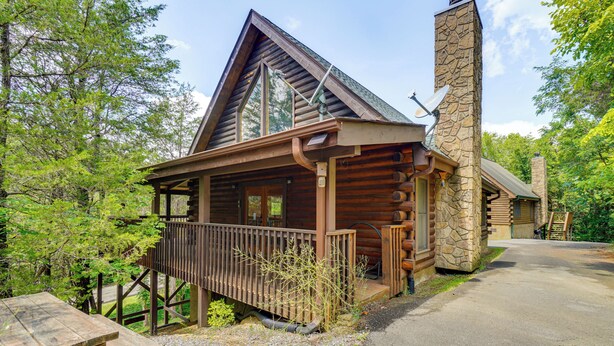 A log cabin with a stone chimney, a covered porch, and a picnic table. - Private Hot Tub: Lake Resort Cabin in Sevierville! (Sevierville)