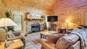 A cozy log cabin interior with a stone fireplace, leather furniture, and a television. - Private Hot Tub: Lake Resort Cabin in Sevierville! (Sevierville)