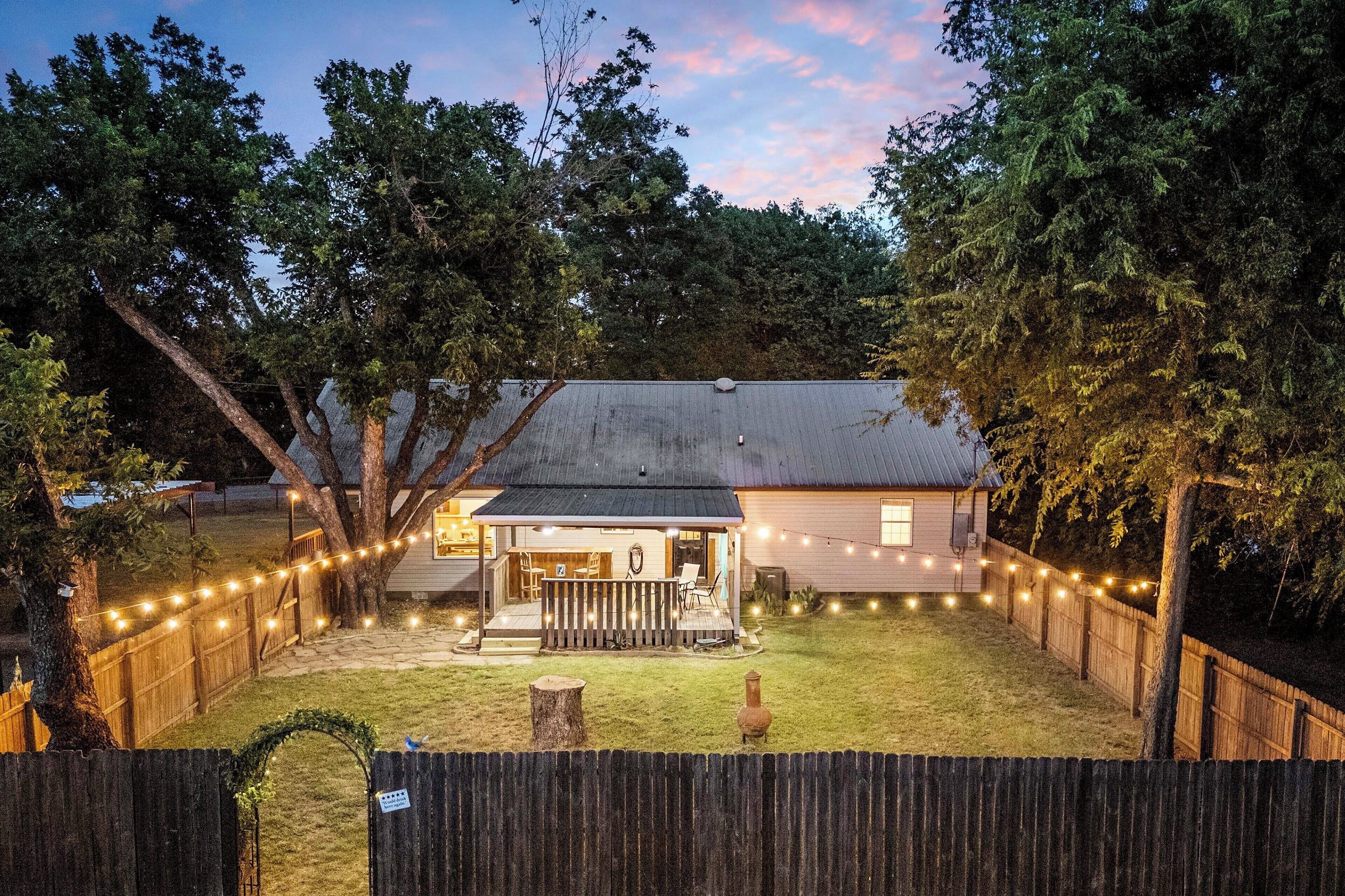 A house with a fenced backyard, a porch with outdoor seating, and string lights.
