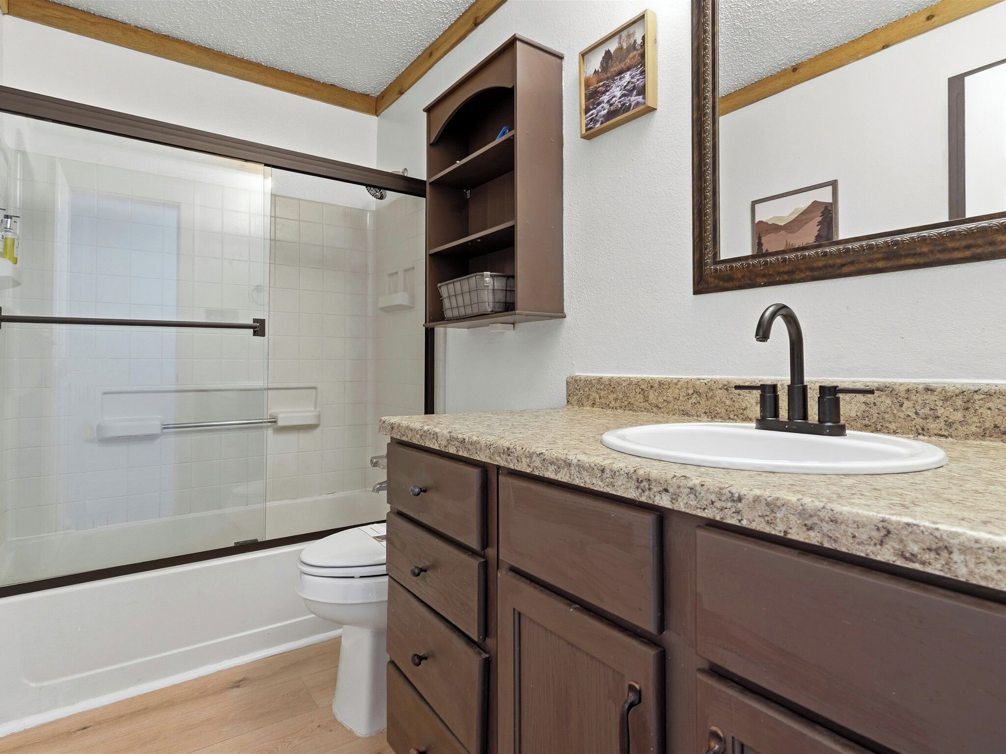 A bathroom with a shower, toilet, sink, and wooden cabinets.