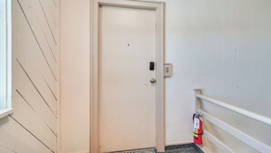 A white door with a handle and a lock, a fire extinguisher mounted on the wall, and a white railing on the right side. - Steps to St Pete Beach: Condo w/ Pool Access (St. Pete Beach)