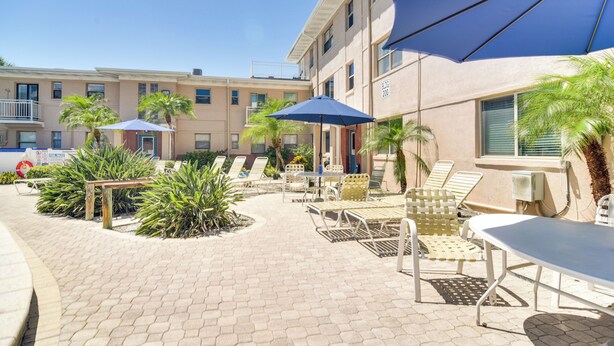 A courtyard with outdoor seating, palm trees, and a building with balconies. - Steps to St Pete Beach: Condo w/ Pool Access (St. Pete Beach)