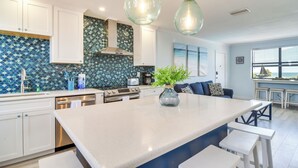 A modern kitchen with white cabinets, a large island, and a blue-tiled backsplash. - Steps to St Pete Beach: Condo w/ Pool Access (St. Pete Beach)