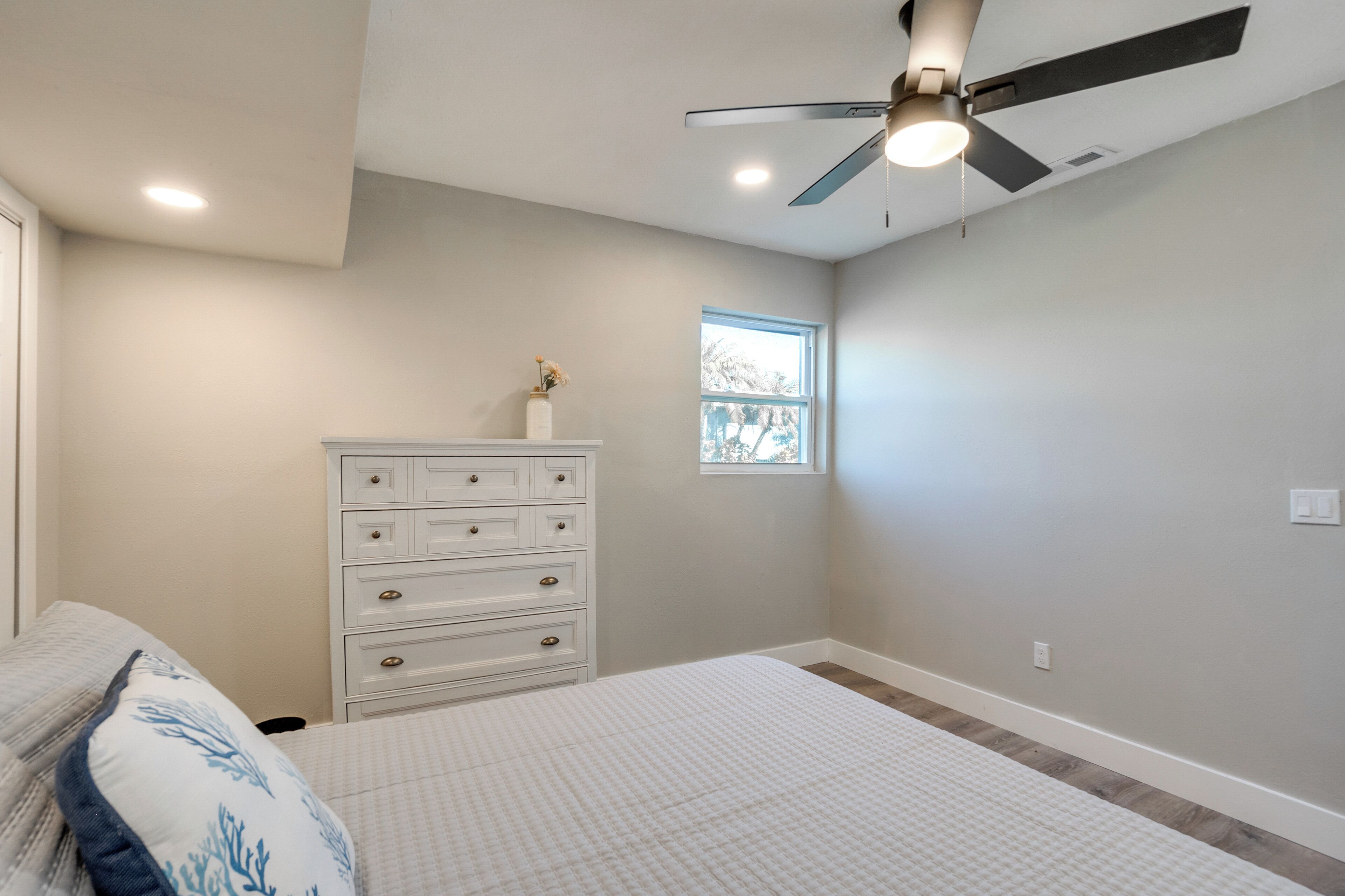 Un dormitorio con cama, cómoda, ventilador de techo y ventana.
