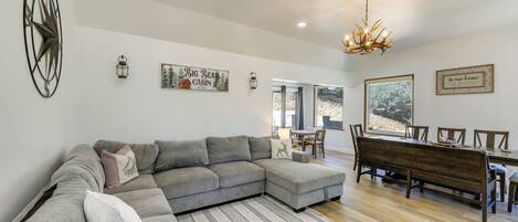A modern living room with a sectional sofa, a dining area with a wooden table and chairs, and decorative wall art.
