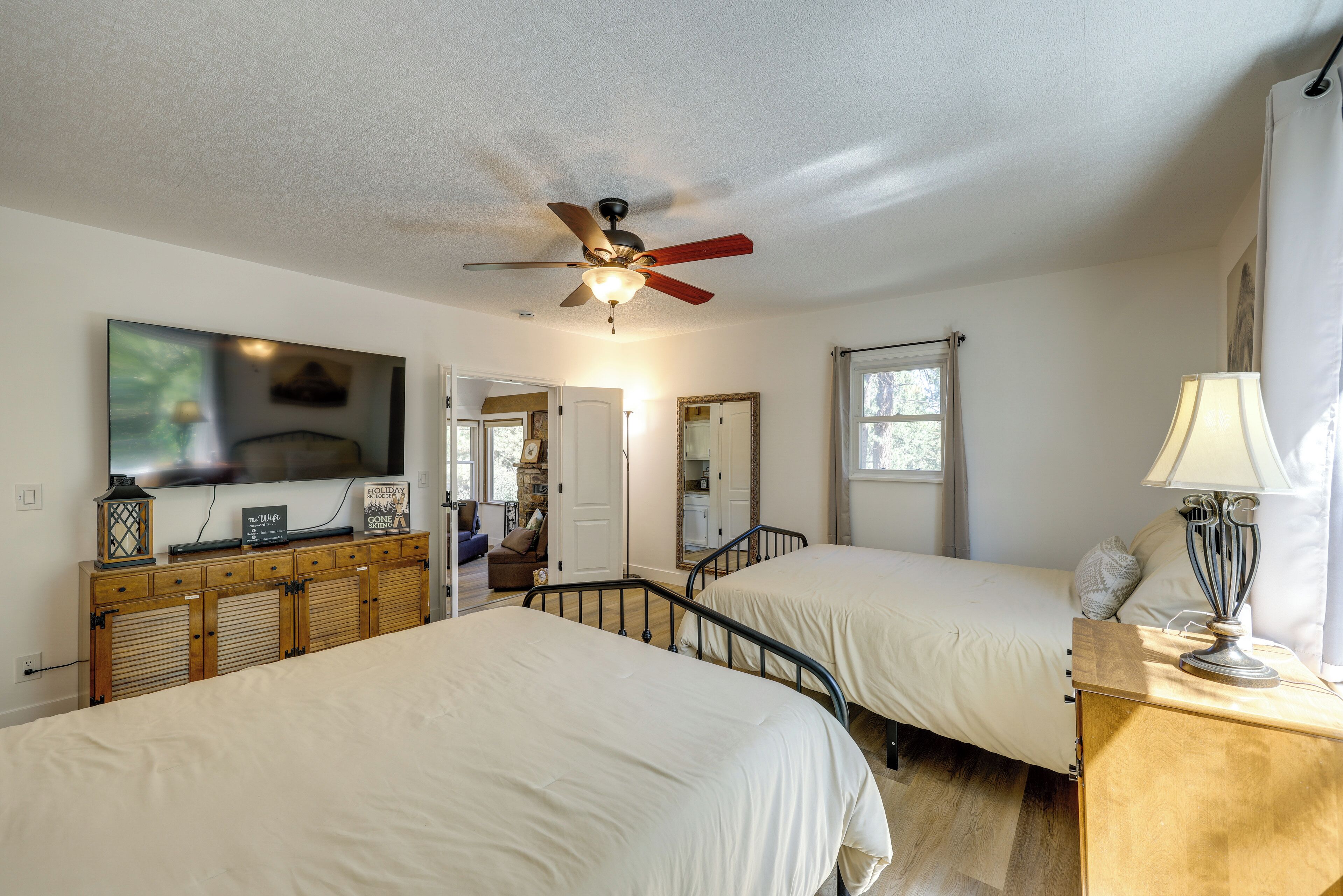 A bedroom with two beds, a ceiling fan, a TV, and a fireplace.
