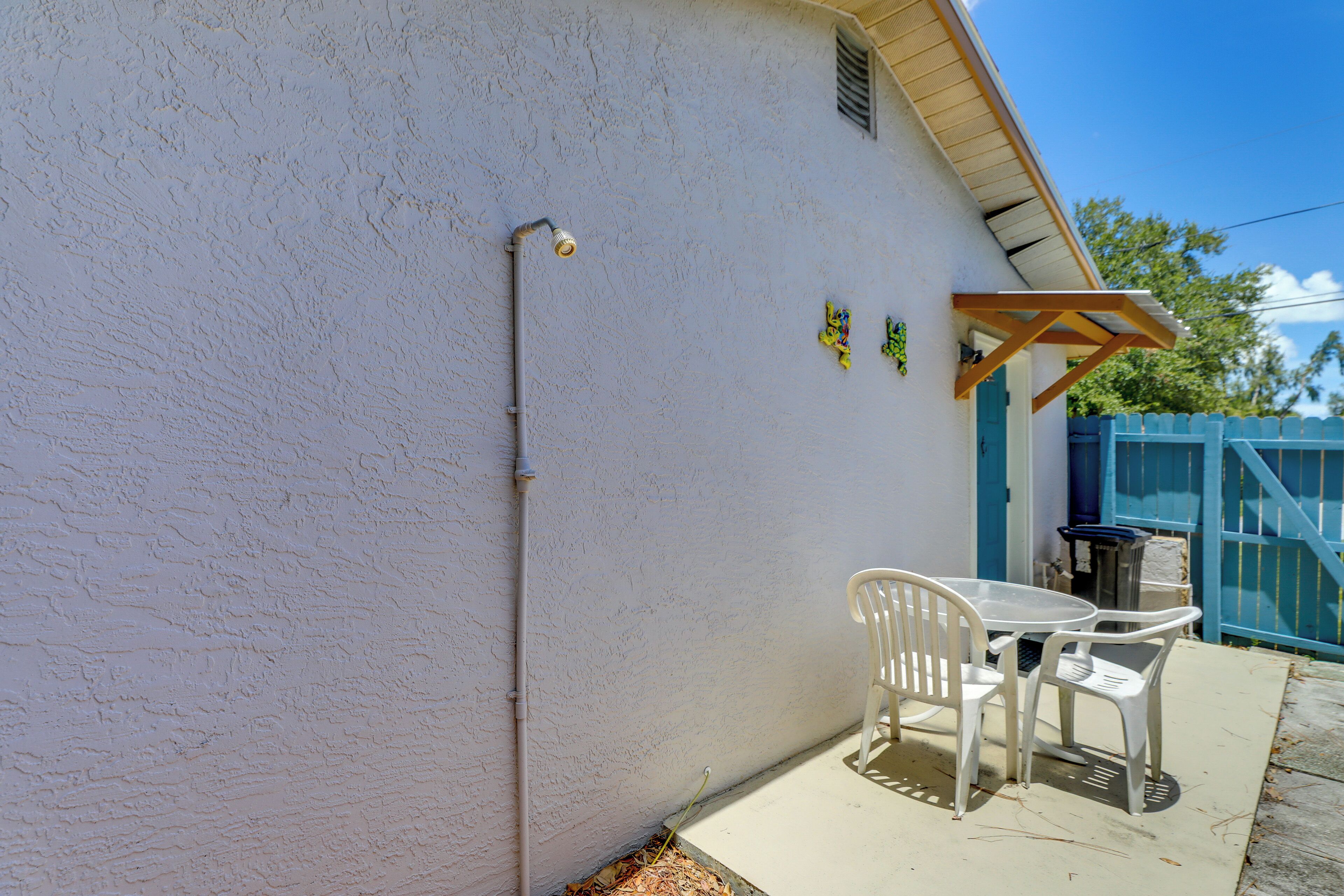 A patio with a white table and chairs, a blue gate, and a white wall with a window and a vent.