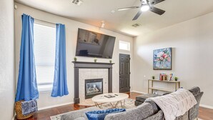 A living room with a fireplace, a flat-screen TV, a ceiling fan, and a sofa.
