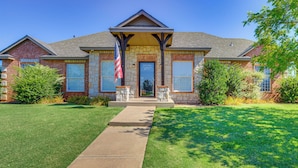 A two-story brick house with a front porch, a flag, and a well-maintained lawn.