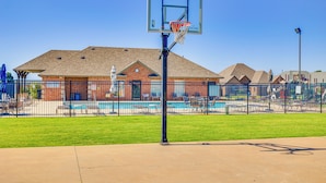 A basketball court with a fence, a pool, and a building in the background.