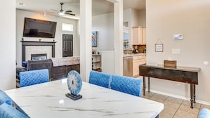 A modern living room with a fireplace, a dining table with blue chairs, and a kitchen area in the background.