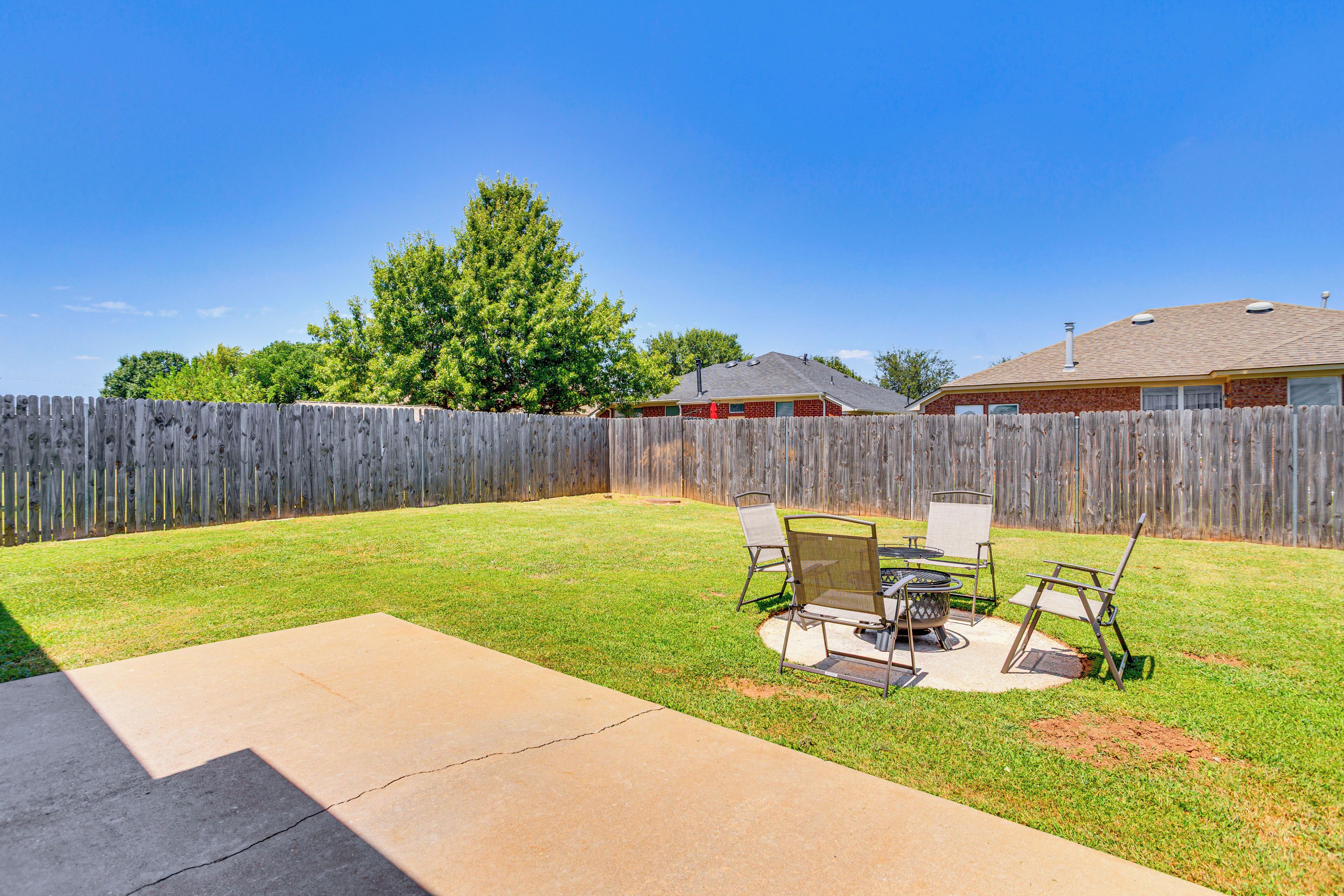 A backyard with a wooden fence, a grassy lawn, and a patio area with outdoor furniture.
